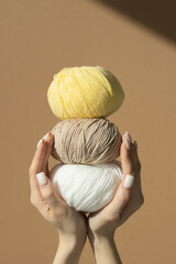 Three balls of knitting thread in women's hands on a brown insulated background in sunlight. Vertical frame.