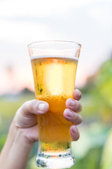 Close-up of hands holding a cold beer glass, condensation forming on the surface, capturing a moment of relaxation, enjoyment