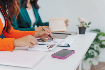 Fototapeta premium Two Asian businesswomen sit together at a desk, working professionally to solve problems. One appears to be the boss