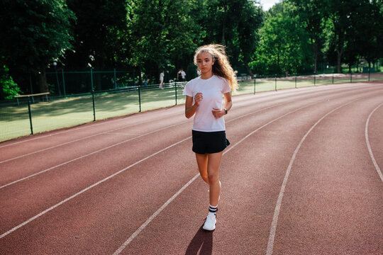 Teenage girl training at the stadium, doing track and field exercises, running and performing various athletic drills.