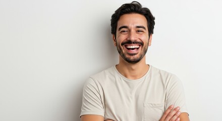 A man with dark hair and a mustache is smiling broadly with his arms crossed against a white background