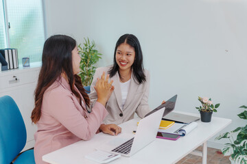 Two Asian businesswomen working together at a desk, focused and professional. They collaborate on...