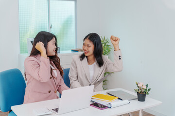 Two Asian businesswomen working together at a desk, focused and professional. They collaborate on...