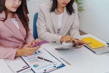 Two Asian businesswomen working together at a desk, focused and professional. They collaborate on...