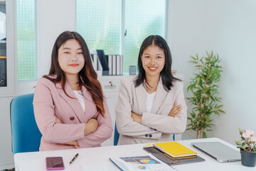 Two Asian businesswomen working together at a desk, focused and professional. They collaborate on...