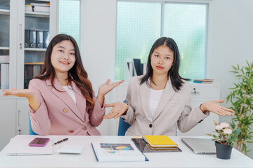 Two Asian businesswomen working together at a desk, focused and professional. They collaborate on...