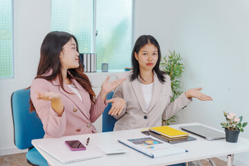 Two Asian businesswomen working together at a desk, focused and professional. They collaborate on...