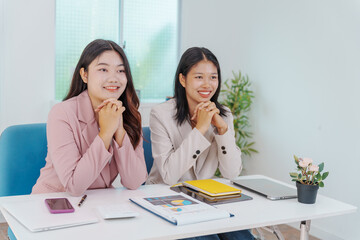 Two Asian businesswomen working together at a desk, focused and professional. They collaborate on...