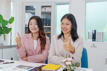 Two Asian businesswomen working together at a desk, focused and professional. They collaborate on...