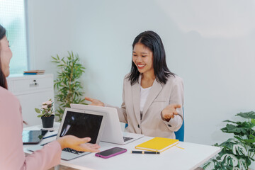 Two Asian businesswomen working together at a desk, focused and professional. They collaborate on...