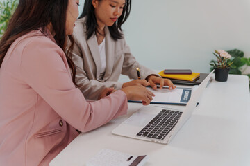 Two Asian businesswomen working together at a desk, focused and professional. They collaborate on...