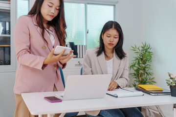 Two Asian businesswomen working together at a desk, focused and professional. They collaborate on...