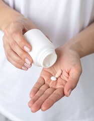 A close-up image of  woman holding supplement pill alongside a white bottle.