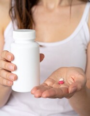 A close-up image of  woman holding supplement pill alongside a white bottle.