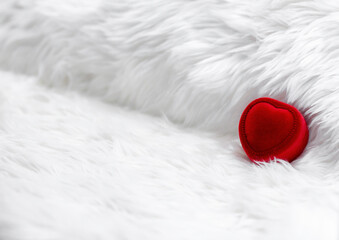 Red heart shaped diamond ring box on fur white blanket.