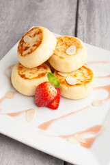 Delicious sweet cottage cheese pancakes served with fresh strawberries and cream on a white plate for breakfast