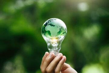 Renewable Energy. Hand holding a Green world on the light bulb on green background. Green energy sources for sustainable Environmental. Clean energy technology and  eco friendly. Earth Day