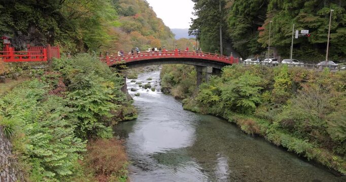 Scenic video capturing the gentle flow of the Daiya River leading up to the traditional red Shinkyo Bridge with visitors enjoying the view amid vibrant autumn foliage in Nikko Japan