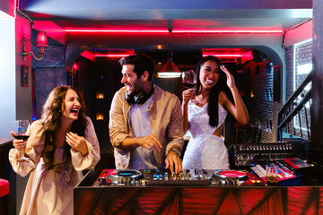 Diverse group of friends enjoying girl’s night out at a nightclub, laughing and dancing near DJ...