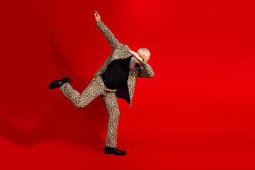 Stylish elderly gentleman in a leopard print suit striking a fun pose against a vibrant red background showcasing charisma and charm