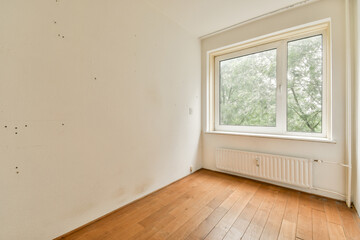 A minimalist empty room featuring a large window that allows natural light, showcasing wooden flooring and a clean, unfinished wall. Ideal for interior design inspiration.