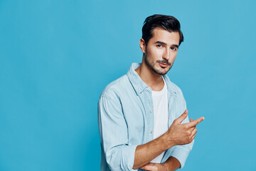 Stylish young man wearing light blue shirt on blue background pointing with finger, expressing...