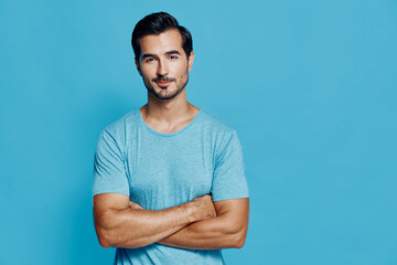 Confident young caucasian man in blue t-shirt stands with arms crossed, smiling at the camera,...