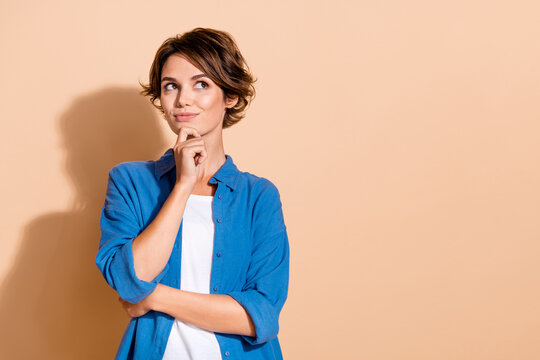 Portrait of young pensive clever lady in blue shirt touch chin looking empty space deep thinking isolated on beige color background