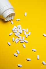 White Pills Spilling from Bottle on Bright Yellow Background