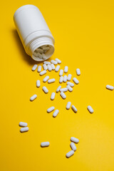 White Pills Spilling from Bottle on Bright Yellow Background