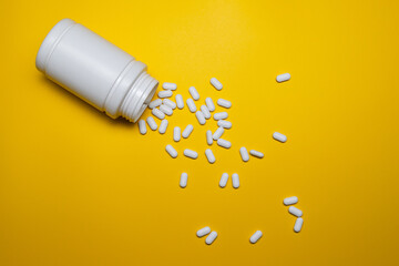 White Pills Spilling from Bottle on Bright Yellow Background