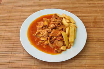 A plate of food with meat and potatoes. The meat is covered in sauce and the potatoes are cut into small pieces