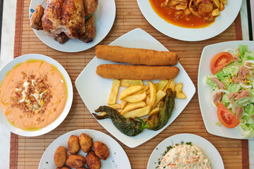 A table with a variety of food including chicken, potatoes, and salad. There are also some bowls and plates on the table