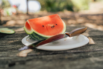 Slice of fresh watermelon on paper plate with knife on rustic wooden table