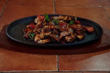 A plate of food with meat and vegetables on a wooden board. The plate is on a table