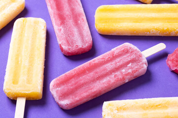 Red strawberry popsicles and yellow popsicles on purple background