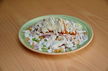 A plate of food with a green plate and a white sauce. The food is chicken and vegetables