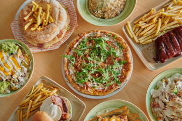 A table with many plates of food including pizza, sandwiches, and fries. The pizza is on the left side of the table