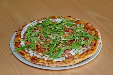 A pizza with spinach and bacon on top. It is sitting on a white plate. The pizza is cut into slices