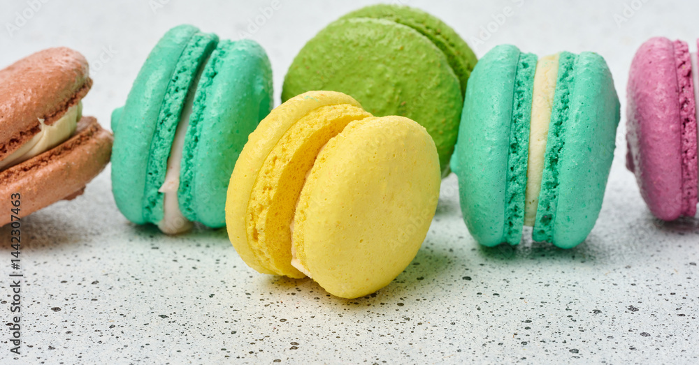 Poster an assortment of colorful macarons on a white surface with dark speckles. the macarons have a smooth