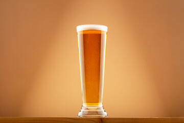 Glass of amber beer with light foam on wooden plank against warm gradient background. Concept of...