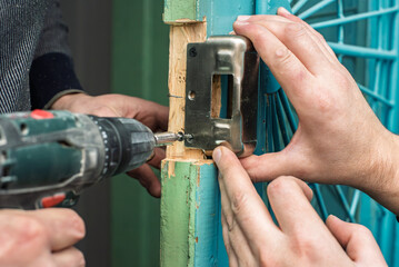 Two repairmen installing new door lock using special tool. Teamwork in action, fixing and installing lock on metal door for safety