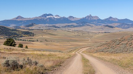Fototapeta premium A dirt road winds through a vast, open landscape, leading towards a majestic mountain range.