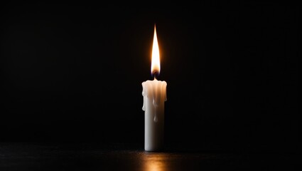 Close-up image of a solitary candle with a burning flame and melted wax on a table, set against a dark background with interior lighting.