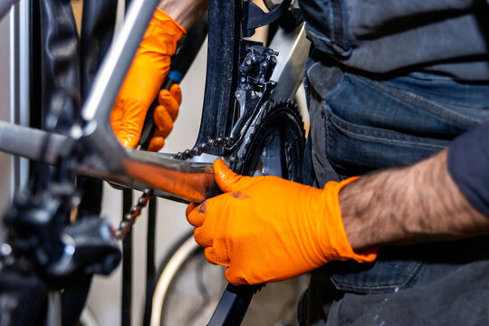Bike mechanic wearing orange gloves repairing bicycle transmission - Powered by Adobe