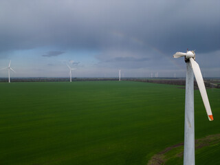 Close-up of a damaged wind turbine blade on a large green field with multiple turbines and cloudy...
