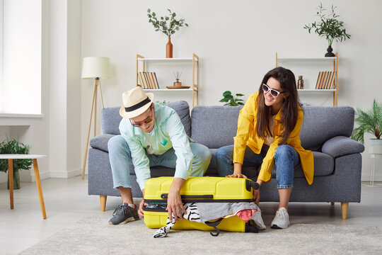 Portrait of a young happy smiling couple man and woman packing suitcase for vacation trip sitting on sofa at home together. Family summer holiday preparations. Travelling and journey concept.