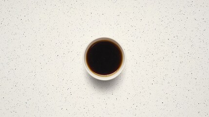 A white cup filled with a dark liquid sits on a speckled white surface.