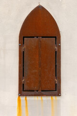 Weathered iron window shutter with rust stains on a textured wall caught in soft natural light