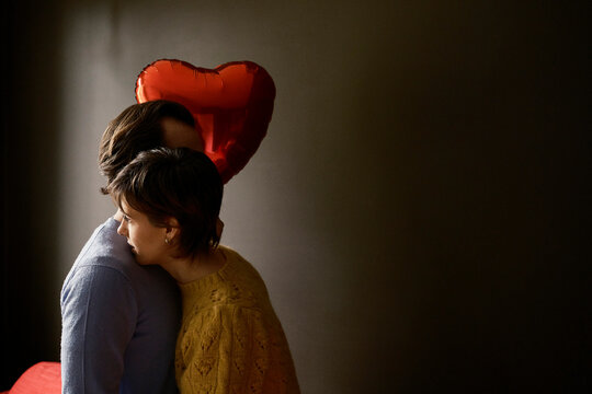 Couple embracing with a heart shaped balloon in a darker room